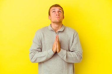 Sarı arka planda izole edilmiş genç beyaz bir adam el ele tutuşup ağız kenarında dua ediyor, kendinden emin hissediyor..