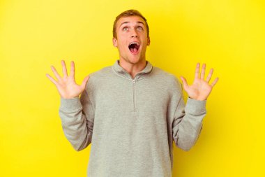 Sarı arka planda izole edilmiş genç beyaz adam gökyüzüne haykırıyor, yukarı bakıyor, hayal kırıklığına uğramış..