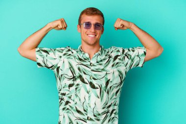 Mavi arka planda izole edilmiş yaz kıyafetleri giyen genç beyaz adam kadınsı gücün sembolü olan kollarıyla güçlü bir hareket sergiliyor.