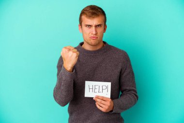 Mavi arka planda yardım levhası tutan genç beyaz bir adam kameraya yumruk ve agresif yüz ifadesini gösteriyor..
