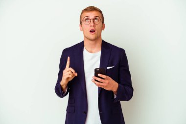 Elinde cep telefonu olan genç bir iş adamı beyaz arka planda izole edilmiş ve ağzı açık bir şekilde üst tarafı işaret ediyor..