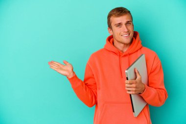 Mavi arka planda dizüstü bilgisayar tutan genç beyaz bir adam bir avuç içinde fotokopi alanı ve belinde bir el daha olduğunu gösteriyor..