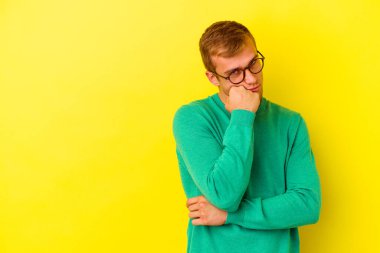 Sarı arka planda izole edilmiş genç, üzgün ve dalgın hisseden, kopyalama alanına bakan beyaz bir adam..