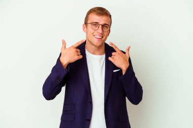 Beyaz arka planda izole edilmiş genç beyaz iş adamı gülümsüyor, parmaklarını ağıza doğrultuyor..