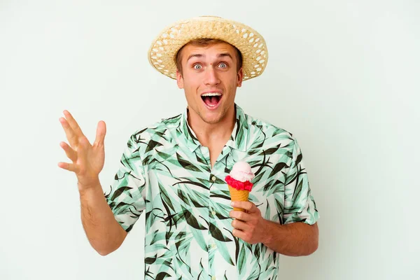若い白人男性が夏服を着て白い背景に隔離されたアイスクリームを持っていて 楽しい驚き 興奮し 手を上げる — ストック写真