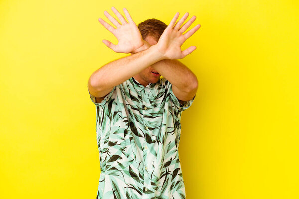 Young caucasian man isolated on yellow background keeping two arms crossed, denial concept.