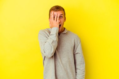 Sarı arka planda izole edilmiş genç beyaz adam yüzünün yarısını palmiye ile örterek eğleniyor..