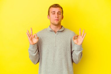 Sarı arka planda izole edilmiş genç beyaz adam sıkı çalışma gününden sonra rahatlıyor. Yoga yapıyor..