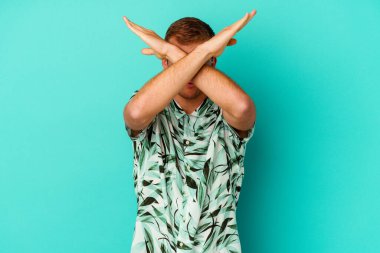 Mavi arka planda izole edilmiş yaz kıyafetleri giyen genç beyaz bir adam iki kolu çapraz tutuyor, inkar kavramı..