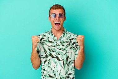 Mavi arka planda soyutlanmış, tasasız ve heyecanlı yaz kıyafetleri giyen genç beyaz bir adam. Zafer konsepti.