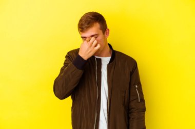 Kafkasyalı genç adam sarı arka planda izole edilmiş, başı ağrıyor, yüzüne dokunuyor..