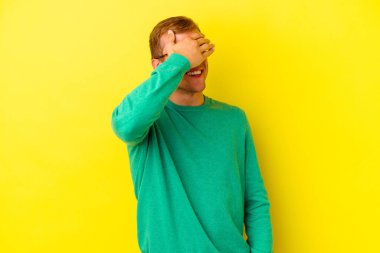 Sarı arka planda izole edilmiş genç beyaz adam ellerini başının üstünde tutarak neşe içinde gülüyor. Mutluluk kavramı.