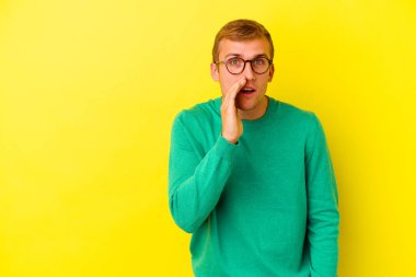 Sarı arka planda izole edilmiş genç beyaz bir adam gizli bir sıcak fren haberi veriyor ve yana bakıyor.