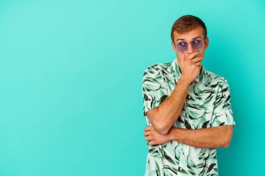 Mavi arka planda izole edilmiş yaz kıyafetleri giyen genç beyaz adam ağzını eliyle kapatan bir fotokopi odasına bakıyor..