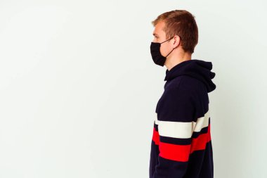 Virüs maskesi takmış beyaz arka planda izole edilmiş beyaz bir adam sola bakıyor, yan pozlar veriyor..