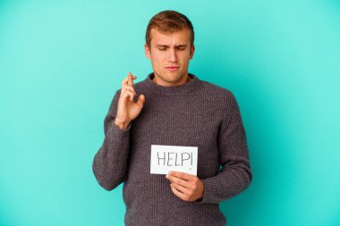 Mavi arka planda izole edilmiş yardım levhası tutan beyaz bir adam şans getirsin diye dua ediyor.