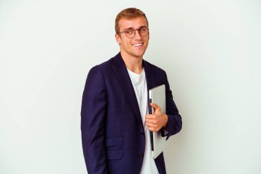 Beyaz arka planda dizüstü bilgisayar tutan beyaz bir genç adam gülümsüyor, neşeli ve keyifli görünüyor..