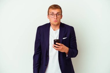 Beyaz arka planda izole edilmiş cep telefonu tutan genç bir iş adamı omuzlarını silker ve gözleri açık kalır..