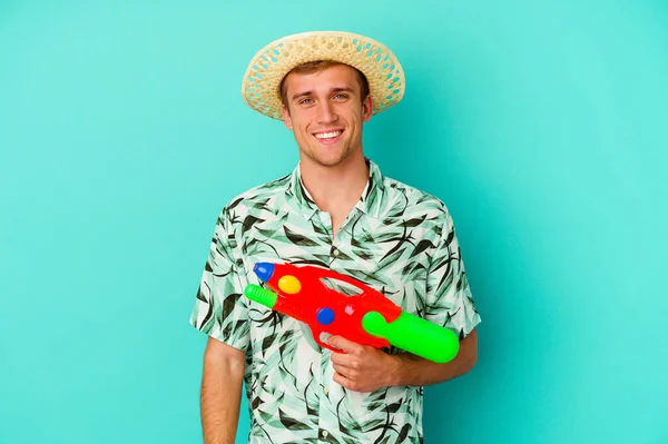 若い白人男性が夏服を着て白い背景に孤立した水鉄砲を持ち 笑顔で陽気な — ストック写真