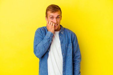 Sarı arka planda izole edilmiş, tırnak yiyen, gergin ve endişeli genç bir beyaz adam..