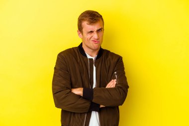 Sarı arka planda izole edilmiş genç beyaz adam alaycı bir ifadeyle kameraya bakıyor..