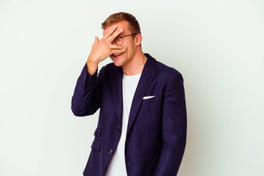 Beyaz arka planda izole edilmiş genç bir beyaz iş adamı kameraya parmaklarıyla göz kırpıyor, yüzünü kapatmaktan utanıyor..