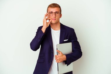 Genç beyaz iş adamı dizüstü bilgisayar tutuyor. Beyaz arka planda izole edilmiş ve parmakları dudaklarında bir sır saklıyor..