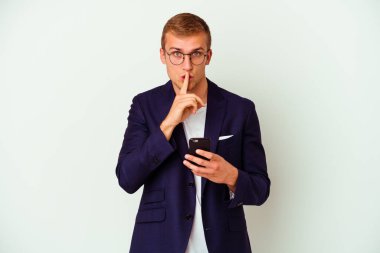 Beyaz arka planda izole edilmiş cep telefonu tutan genç bir iş adamı ya sır saklıyor ya da sessizlik istiyor..
