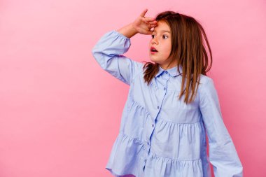 Pembe arka planda izole edilmiş küçük beyaz kız uzaklara bakıyor ve elini alnına koyuyor..