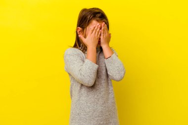 Sarı arka planda izole edilmiş küçük beyaz kız elleriyle gözlerini kapatmaktan korkuyor..