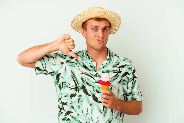 夏服を着た若い白人男性が白い背景に隔離されたアイスクリームを持ち 嫌なジェスチャー 親指を下に示しています 意見の相違 — ストック写真