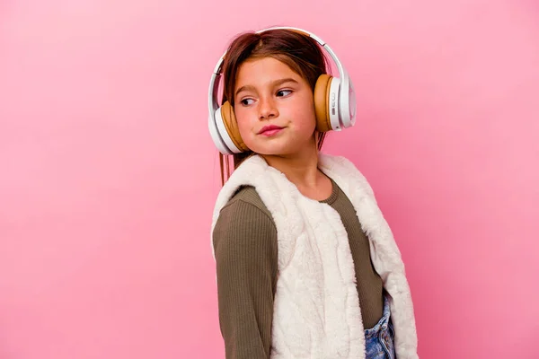 Маленькая Кавказская Девочка Слушает Музыку Изолированную Розовом Фоне Смотрит Сторону — стоковое фото