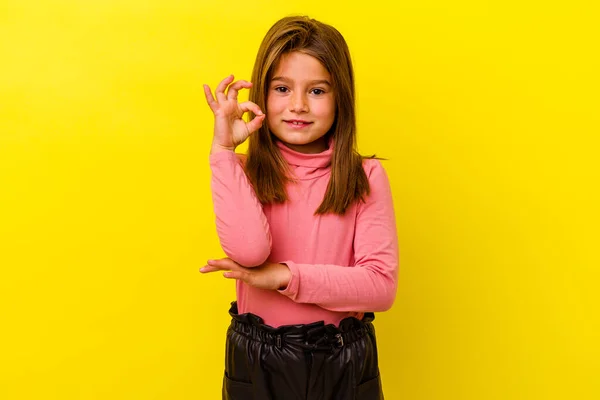 黄色の背景に隔離された小さなCaucasian女の子ウィンクA目と保持しています正しいジェスチャーとともに手 — ストック写真