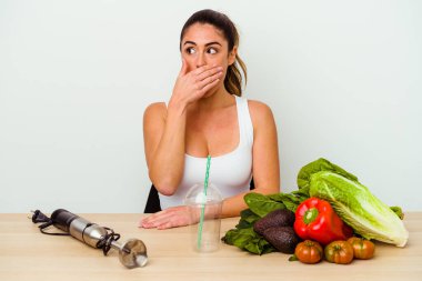 Genç beyaz kadın sebzeli sağlıklı bir smoothie hazırlıyor. Ağzını eliyle kapatan bir fotokopi odasına özenle bakıyor..