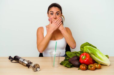Genç, beyaz bir kadın sebzeli sağlıklı bir smoothie hazırlıyor. Ağzını elleriyle kapatıyor..