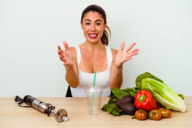 Genç beyaz kadın sebzeli sağlıklı bir smoothie hazırlıyor. Kameraya sarıldığı için kendini güvende hissediyor..