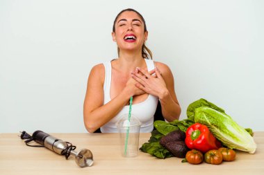Genç, beyaz bir kadın sebzeli sağlıklı bir smoothie hazırlıyor. Gülüyor, elini kalbe koyuyor, mutluluk kavramını koruyor..