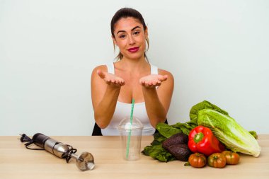 Genç beyaz bir kadın sebzeli sağlıklı bir smoothie hazırlıyor. Elinde avuç içi olan bir şey var ve kameraya sunuyor..