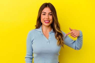 Sarı arka planda izole edilmiş genç beyaz bir kadın gömleğin fotokopi odasını elle işaret ediyor, gururlu ve kendinden emin.