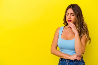 Sarı arka planda izole edilmiş genç beyaz kadın şüpheli ve şüpheci bir ifadeyle yana bakıyor..