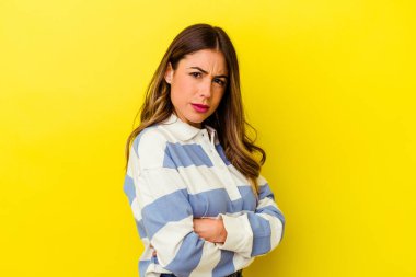 Sarı arka planda izole edilmiş, hoşnutsuzca kaşlarını çatmış, kollarını kavuşturmuş genç beyaz bir kadın..