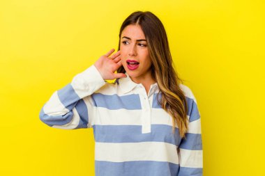 Sarı arka planda izole edilmiş genç beyaz kadın bir dedikoduyu dinlemeye çalışıyor..