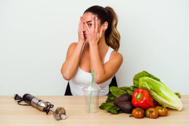 Genç, beyaz bir kadın sebzeli sağlıklı bir smoothie hazırlıyor. Korkmuş ve gergin parmaklarıyla göz kırpıyor..