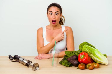 Genç beyaz kadın, yanında sebzeler olan sağlıklı bir smoothie hazırlıyor.