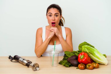 Genç, beyaz bir kadın sebzeli sağlıklı bir smoothie hazırlıyor şans için dua ediyor, şaşırıyor ve ağzını açıyor..