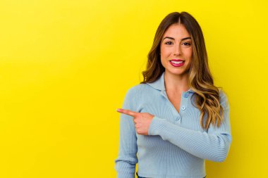 Sarı arka planda izole edilmiş genç beyaz kadın gülümsüyor ve boş alanda bir şeyler gösteriyor..