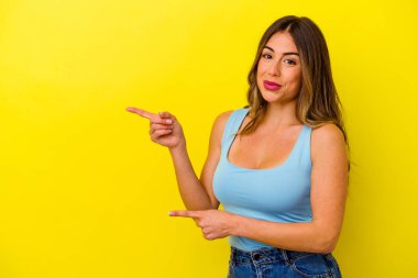 Sarı arka planda izole edilmiş genç beyaz kadın işaret parmaklarıyla fotokopi alanını işaret ederek heyecan ve arzusunu ifade ediyor..