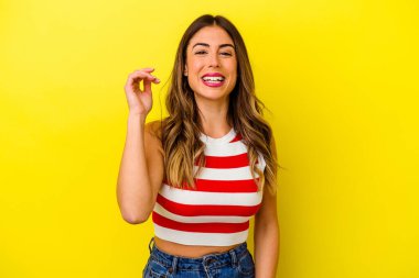 Sarı arka planda izole edilmiş genç beyaz kadın bir şeye gülüyor, elleriyle ağzını kapatıyor..