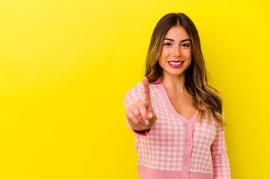 Sarı arka planda izole edilmiş genç beyaz kadın parmak ile bir numarayı gösteriyor..