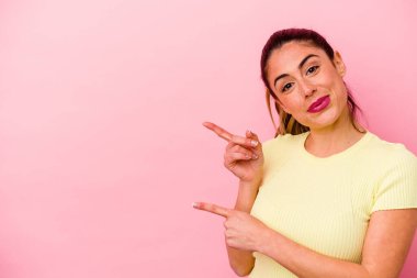 Kafkasyalı genç bir kadın pembe arka planda izole edilmiş kafasının arkasına dokunuyor, düşünüyor ve bir seçim yapıyor..